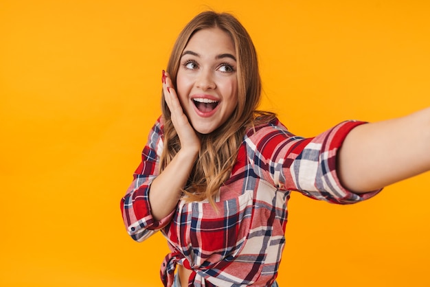 Feliz mujer atractiva joven vistiendo camisa a cuadros sonriendo mientras toma selfie aislado