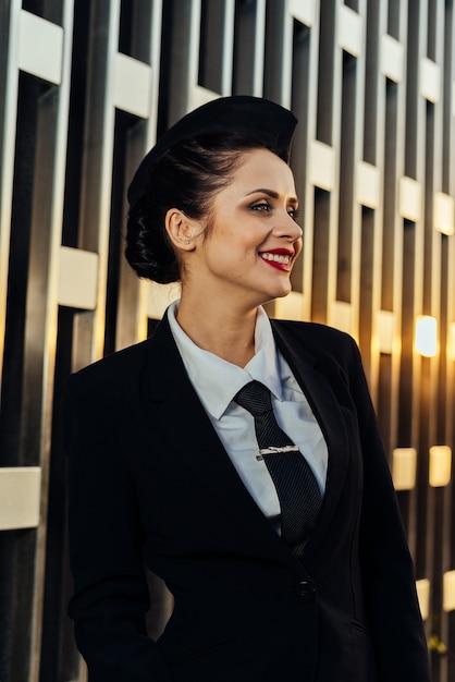 Feliz mujer azafata en uniforme posando sobre fondo de edificio