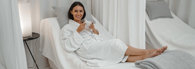 Feliz mujer bonita disfrutando mientras descansa con una taza de café en el salón de spa