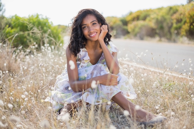 Feliz mujer bonita sentada en el césped en vestido de flores