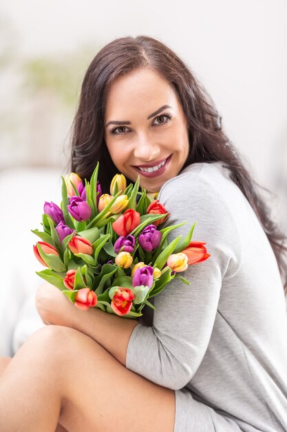 Foto feliz mujer de cabello oscuro sosteniendo un hermoso ramo lleno de tulipanes durante el día nacional de la mujer.