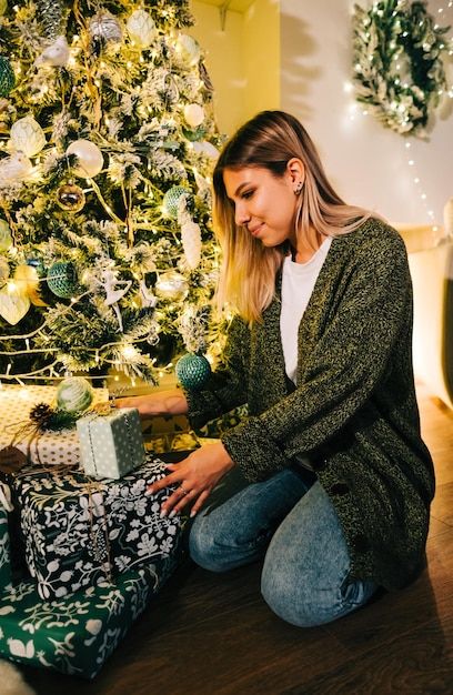 Foto feliz mujer caucásica pone presente bajo el árbol de navidad mientras está sentado en el suelo en casa.