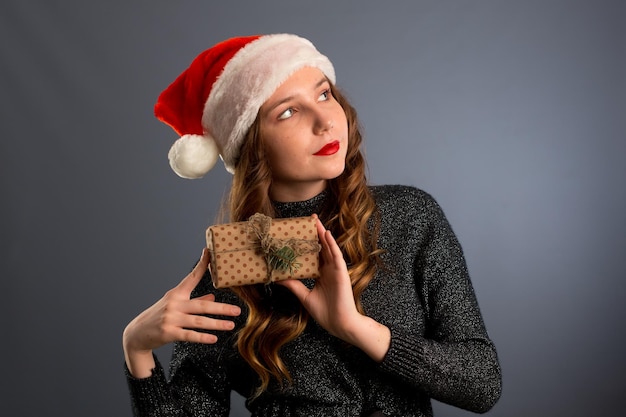 Feliz mujer caucásica de Santa está sonriendo y sosteniendo una caja de regalo para Navidad o Año Nuevo concepto de vacaciones aislado en fondo gris