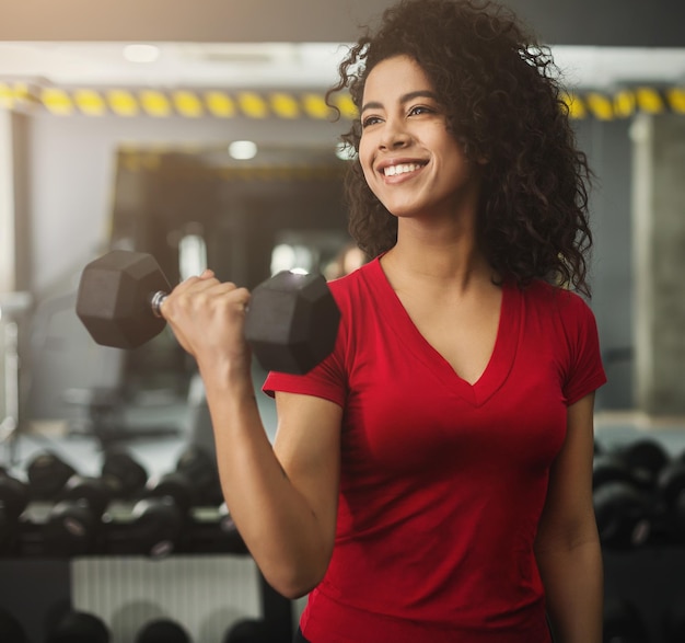 Foto feliz mujer delgada haciendo ejercicios con mancuernas en el gimnasio moderno