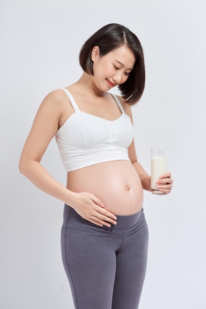 Feliz mujer embarazada bebiendo un vaso de leche fresca y tocando su vientre