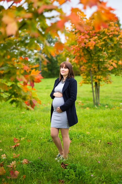 Feliz mujer embarazada caminando en el parque otoño