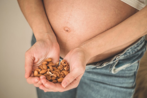 Feliz mujer embarazada en casa comiendo nueces frescas - almendras, nueces. Concepto de embarazo saludable.