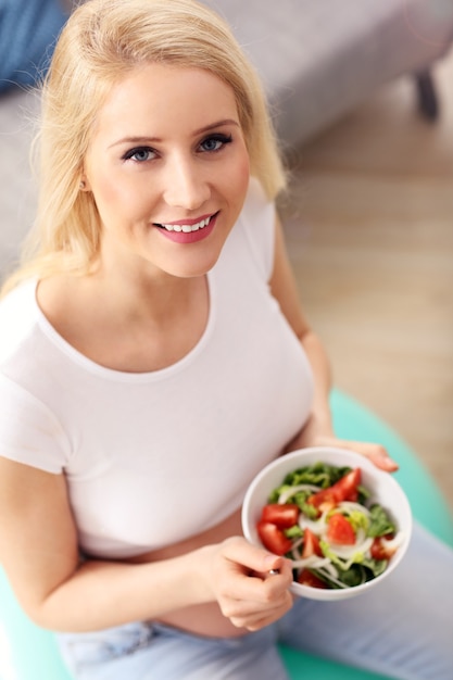 Feliz mujer embarazada comiendo ensalada en casa