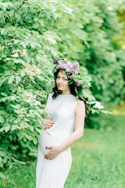 Feliz mujer embarazada en una corona de flores y un ramo de flores silvestres