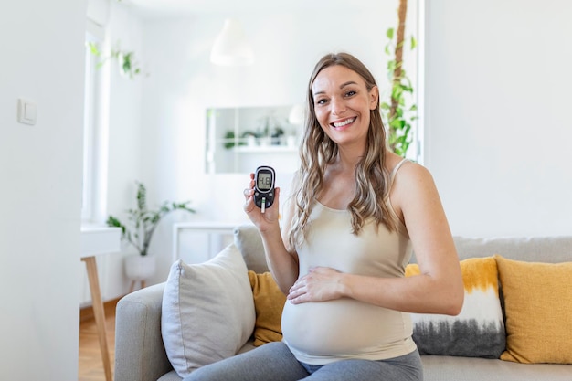 Feliz mujer embarazada con glucómetro comprobando el nivel de azúcar en sangre en casa. Prueba de mujer para detectar niveles altos de azúcar en sangre. Dispositivo de sujeción de mujer embarazada para medir el azúcar en sangre