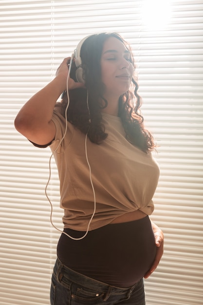 Feliz mujer embarazada con pelo rizado escuchando música en auriculares