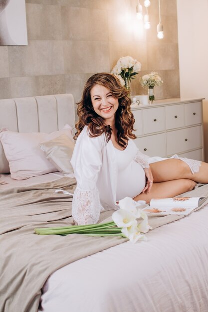 Feliz mujer embarazada sentada en una cama con flores publicidad clínica Cuidado de la salud de la mujer