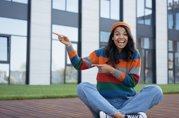 Feliz mujer emocionada señalando con el dedo a un lado y sentado al aire libre