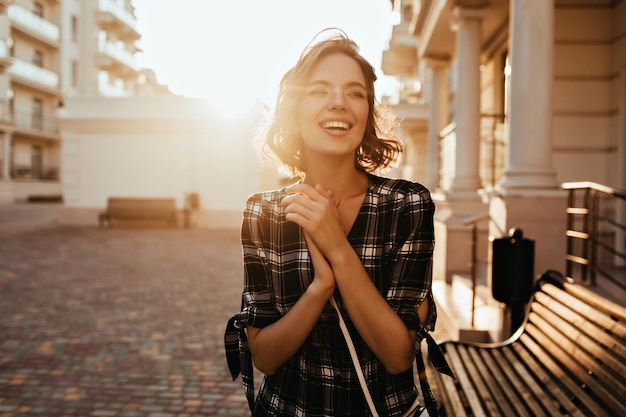 Feliz mujer europea de pie en la calle y disfrutando de la luz del sol Retrato al aire libre de una dama alegre con el pelo corto y ondulado