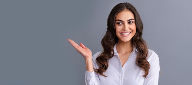 Feliz mujer gerente profesional muestra la mano abierta para el espacio de copia fondo gris que presenta el producto Banner de retrato de cara aislada de mujer con espacio de copia simulada
