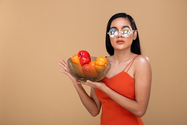 Feliz mujer india asiática con el pelo largo y negro y una gran sonrisa de dientes sosteniendo Apple en la mano y una cesta con frutas frescas saludables y una sonrisa de dientes blancos. Espacio de copia de fondo amarillo beige