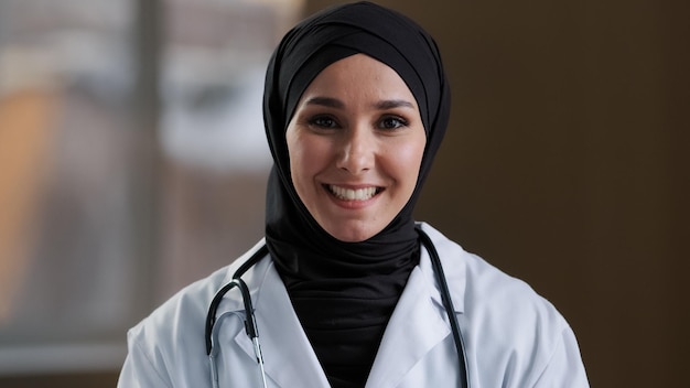 Feliz mujer islámica musulmana doctora practicante árabe asesora en hijab mira la cámara web médica