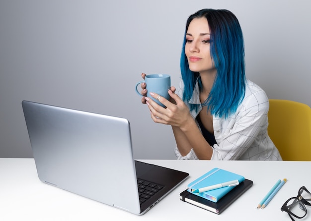 Feliz mujer joven con cabello azul beber café o té relajarse con laptop