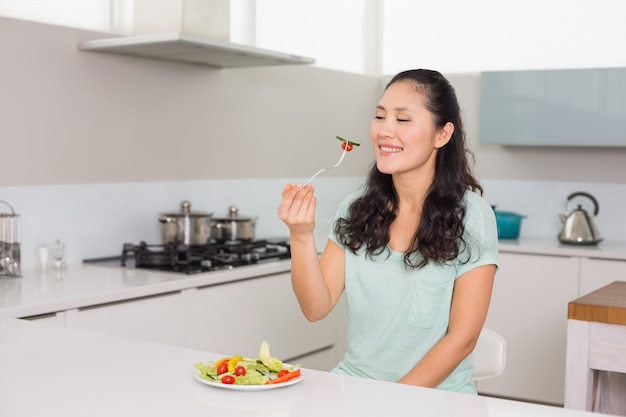 Feliz mujer joven comiendo ensalada en la cocina