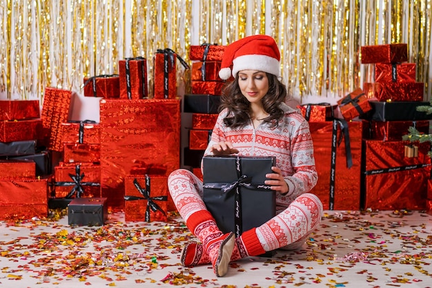 Feliz mujer joven emocionada con sombrero de santa claus con caja de regalo en casa en el piso