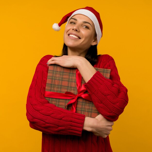 Feliz mujer joven emocionada con sombrero de santa claus con caja de regalo sobre fondo amarillo - imagen