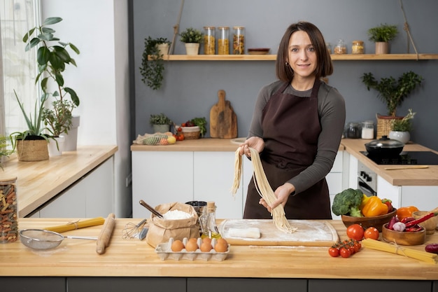 Feliz mujer joven con espaguetis hervidos de pie junto a la mesa de la cocina