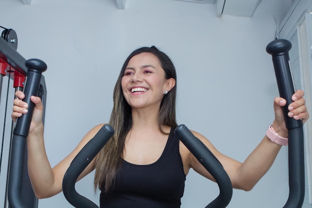 Foto feliz mujer joven hermosa haciendo ejercicio de carrera en una máquina en el gimnasio