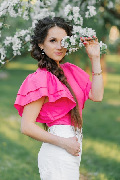 Feliz a una mujer joven y hermosa en un jardín de primavera sosteniendo una rama de flores de manzana y sonriendo