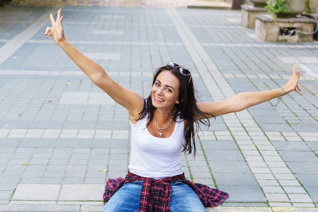 Foto feliz mujer joven de moda sentada en la calle acera modelo femenino elegante