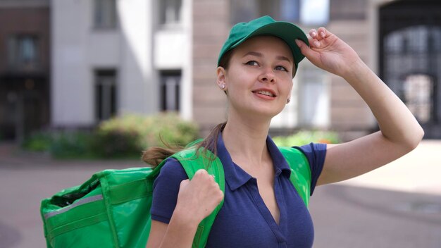 Foto feliz mujer joven o adolescente mensajero en uniforme verde con una gran bolsa térmica o mochila entregar