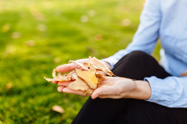 Feliz mujer joven en el parque, niña al aire libre en otoño, sentada en el suelo, con hojas de otoño en sus manos