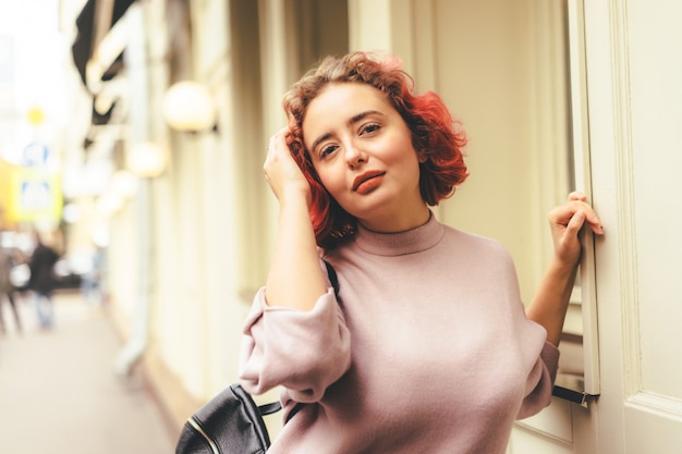 Feliz mujer joven con pelo rojo en vestido morado en un día soleado en la ciudad