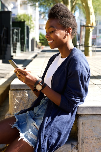 Feliz mujer joven sentada al aire libre y con teléfono celular