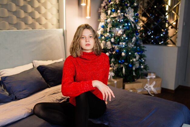 Feliz mujer joven sorprendida emocional por un árbol de Navidad en la acogedora sala de estar, concepto de felicidad