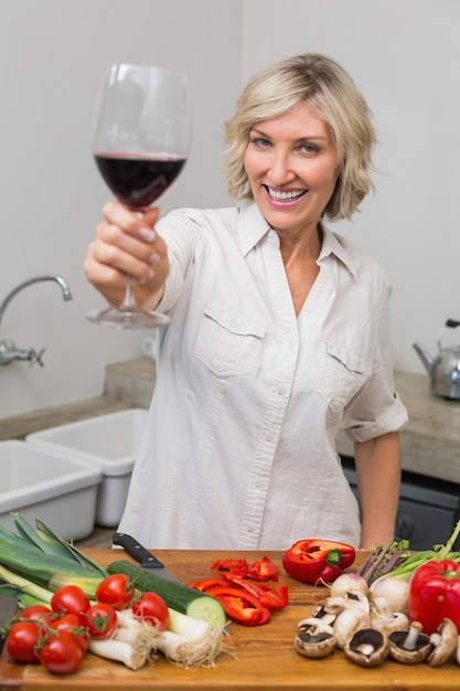 Feliz mujer madura con verduras y copa de vino en la cocina