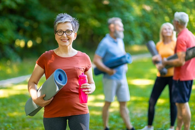 Foto feliz mujer mayor deportiva posando al aire libre mientras entrena con un grupo de amigos