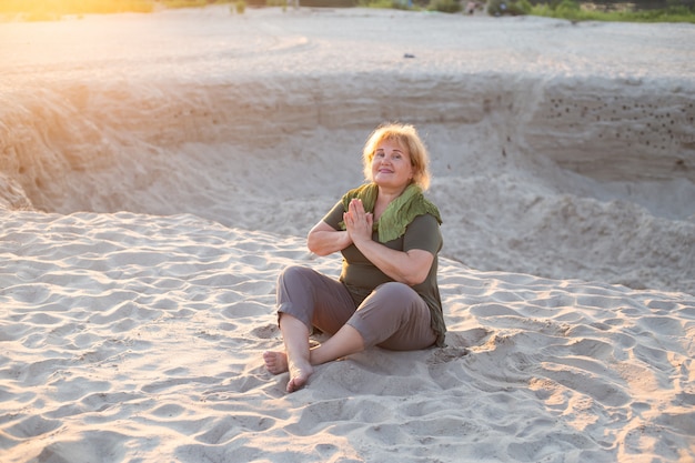 Feliz mujer mayor meditar en una arena afuera en verano