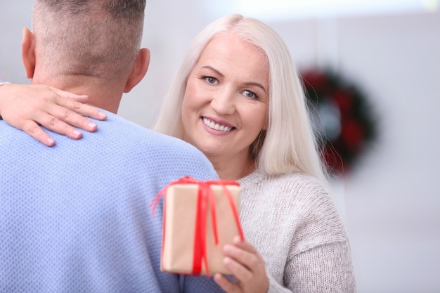 Feliz mujer mayor con regalo de Navidad abrazando a su marido en casa