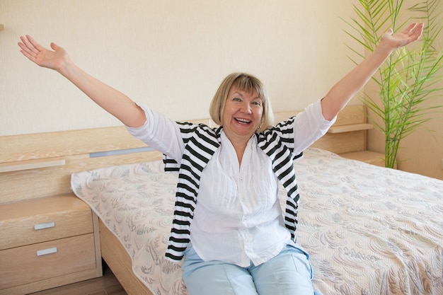 Feliz mujer mayor relajante sonriendo extendió sus manos sobre el fondo de la cama en la casa