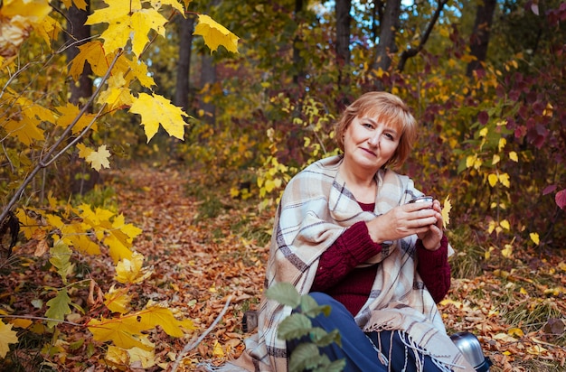 Feliz mujer de mediana edad bebe té en el bosque de otoño