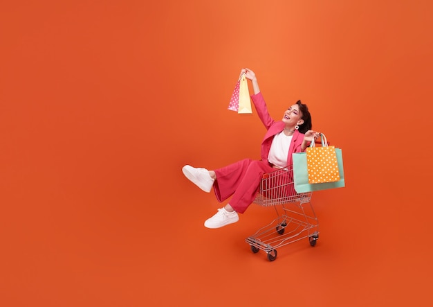 feliz mujer de moda sentada en el carrito y bolsas de compras con promoción de compras venta de verano