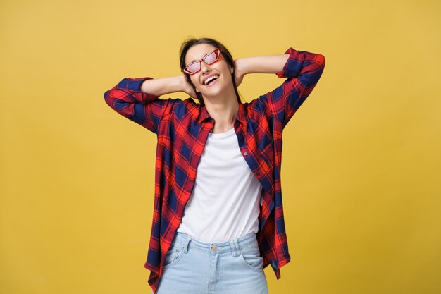 Feliz mujer moderna con estilo con gafas de sol con forma moderna riendo mirando a cámara aislada sobre fondo amarillo. Concepto de felicidad