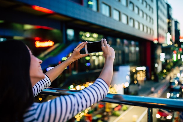 Feliz mujer morena atractiva sonriente hace selfie en su teléfono inteligente en el fondo de la ciudad de noche