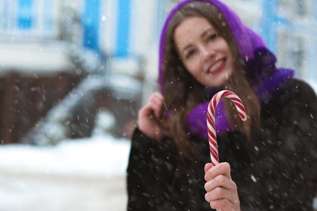 Feliz mujer morena divirtiéndose con paletas de colores en la calle con copos de nieve. Espacio para texto