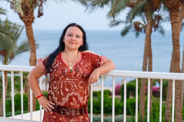 Feliz mujer morena se encuentra en el balcón con el fondo del mar.