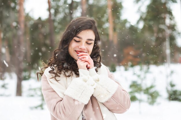 Feliz mujer morena rizada viste abrigo caminando en el bosque durante las nevadas. Espacio vacio