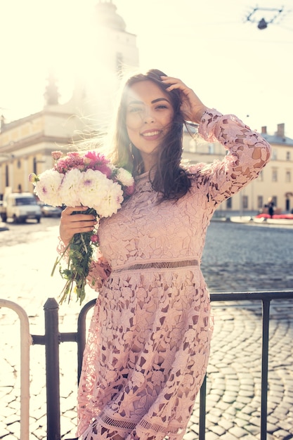 Feliz mujer morena vestida de moda posando en la calle con la llamarada del sol. Efecto tonificante vintage