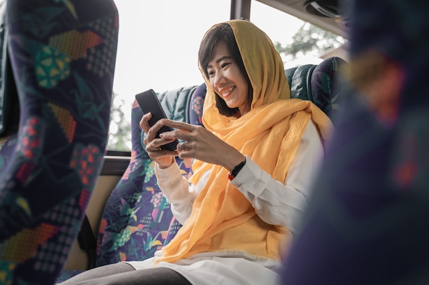 Feliz mujer musulmana usando su teléfono móvil mientras viaja en un autobús para volver a casa