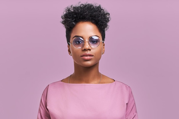 Feliz mujer de negocios afroamericana con una sonrisa positiva, tiene el cabello oscuro y nítido, se regocija de tener un fin de semana y un buen descanso después de una semana agotadora de trabajo duro, aislada en una pared de lavanda