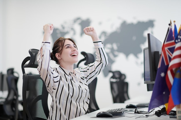 feliz mujer de negocios casual celebrando el éxito mientras trabaja en una computadora de escritorio en el moderno interior de la oficina de inicio de planta abierta